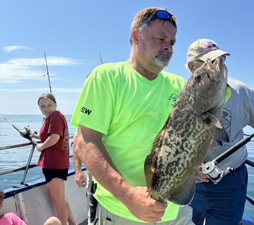 Man in neon shirt holding a large fish on a boat with others fishing.